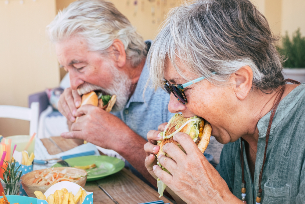 two seniors with grey hair eating fast food at an outdoor table