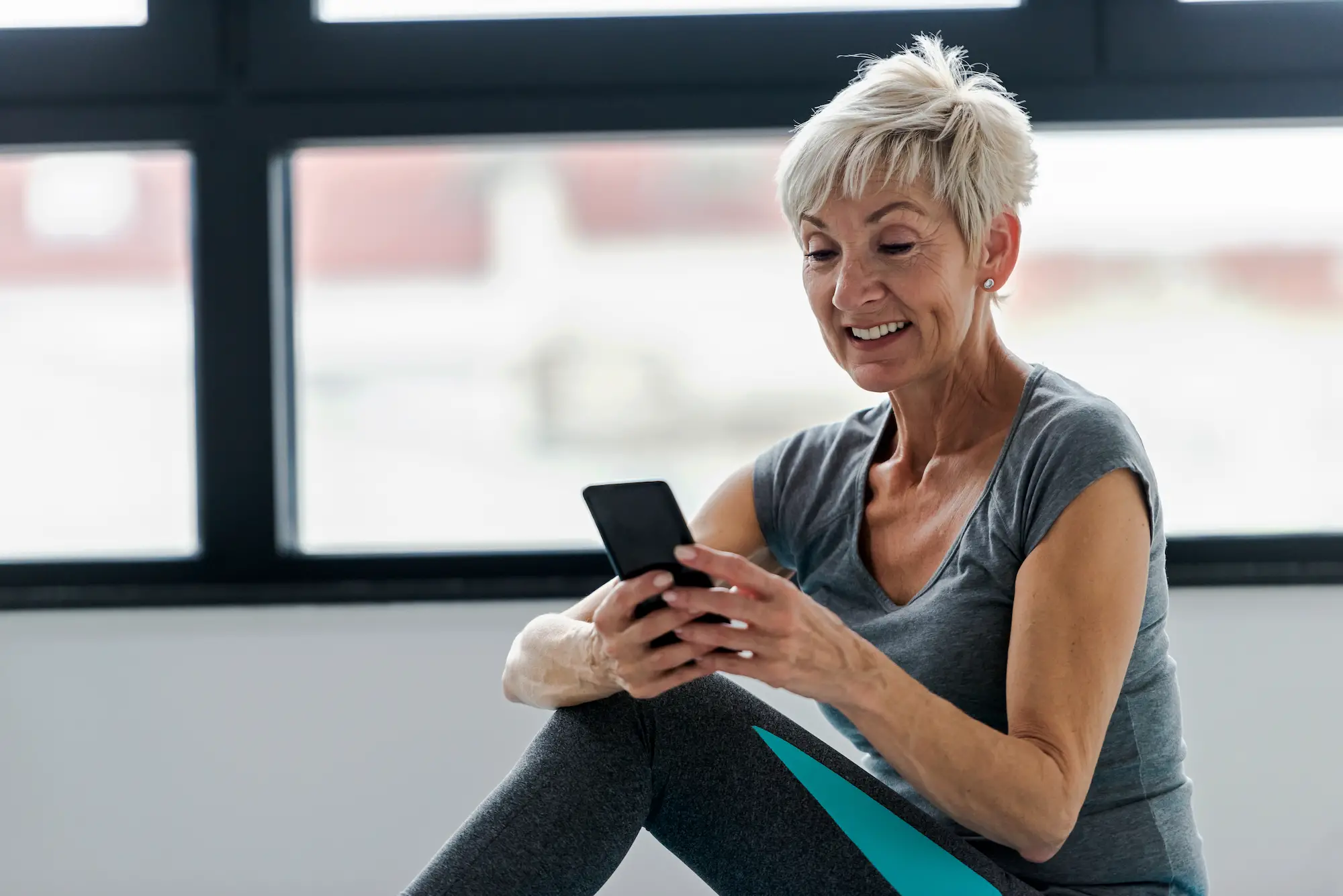 older woman looking at smartphone in gym clothes