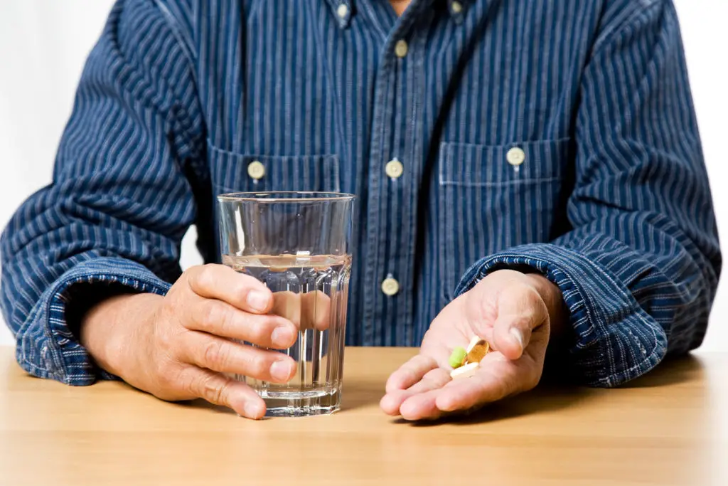 A man takes a handful of pills with water.