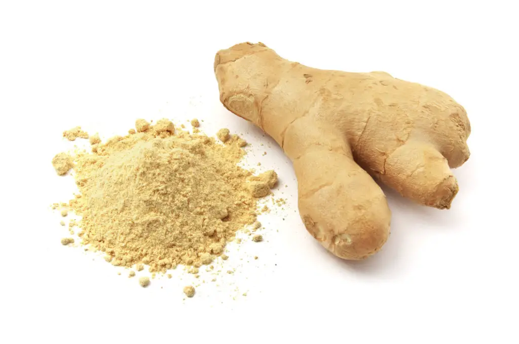 Ginger powder next to a fresh ginger root. 