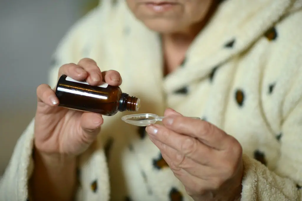 A senior woman takes a spoonful of medication. 