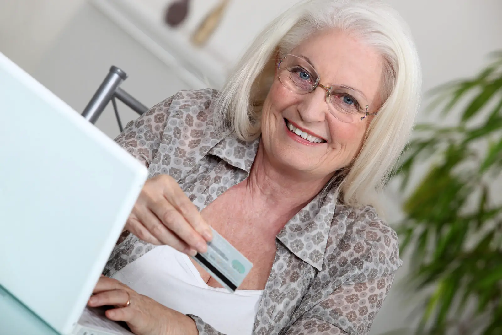 Senior woman at a home computer smiling with a card in her hand about to make a purchase