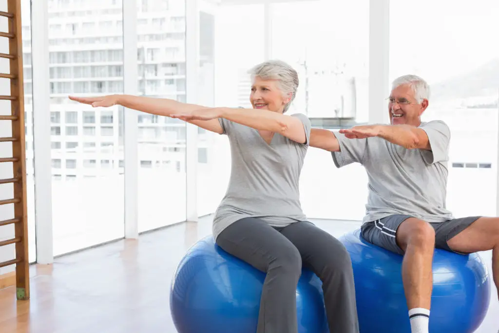 A senior couple stretches on exercise balls. 