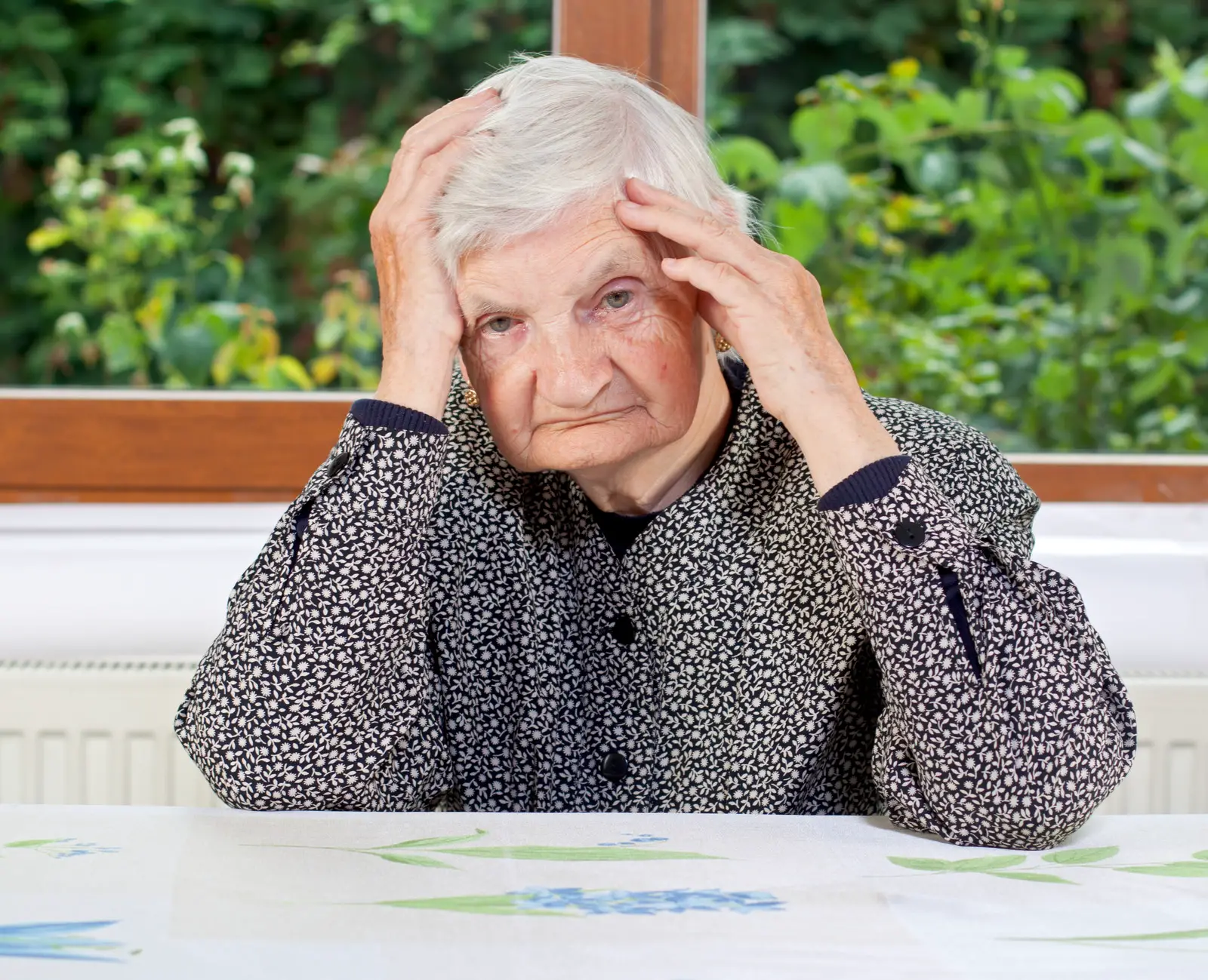 Unhappy senior woman sitting at the table looking confused