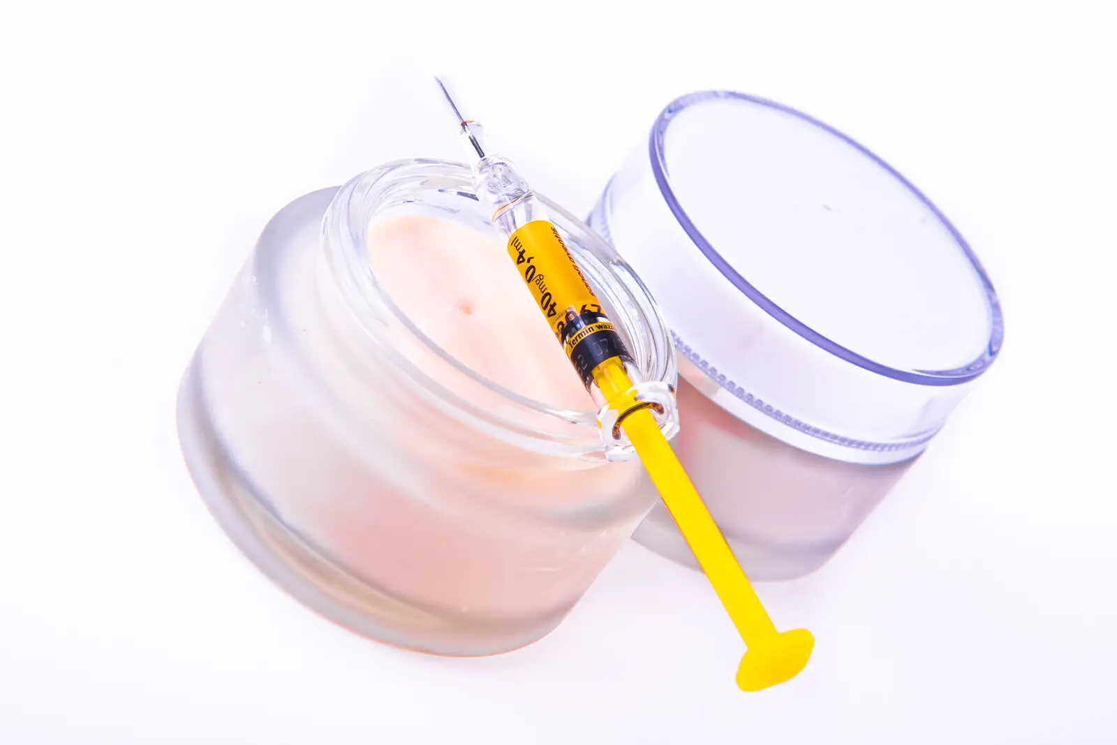 Two jars of anti-aging cream with a botox syringe laying across the top of the open jar