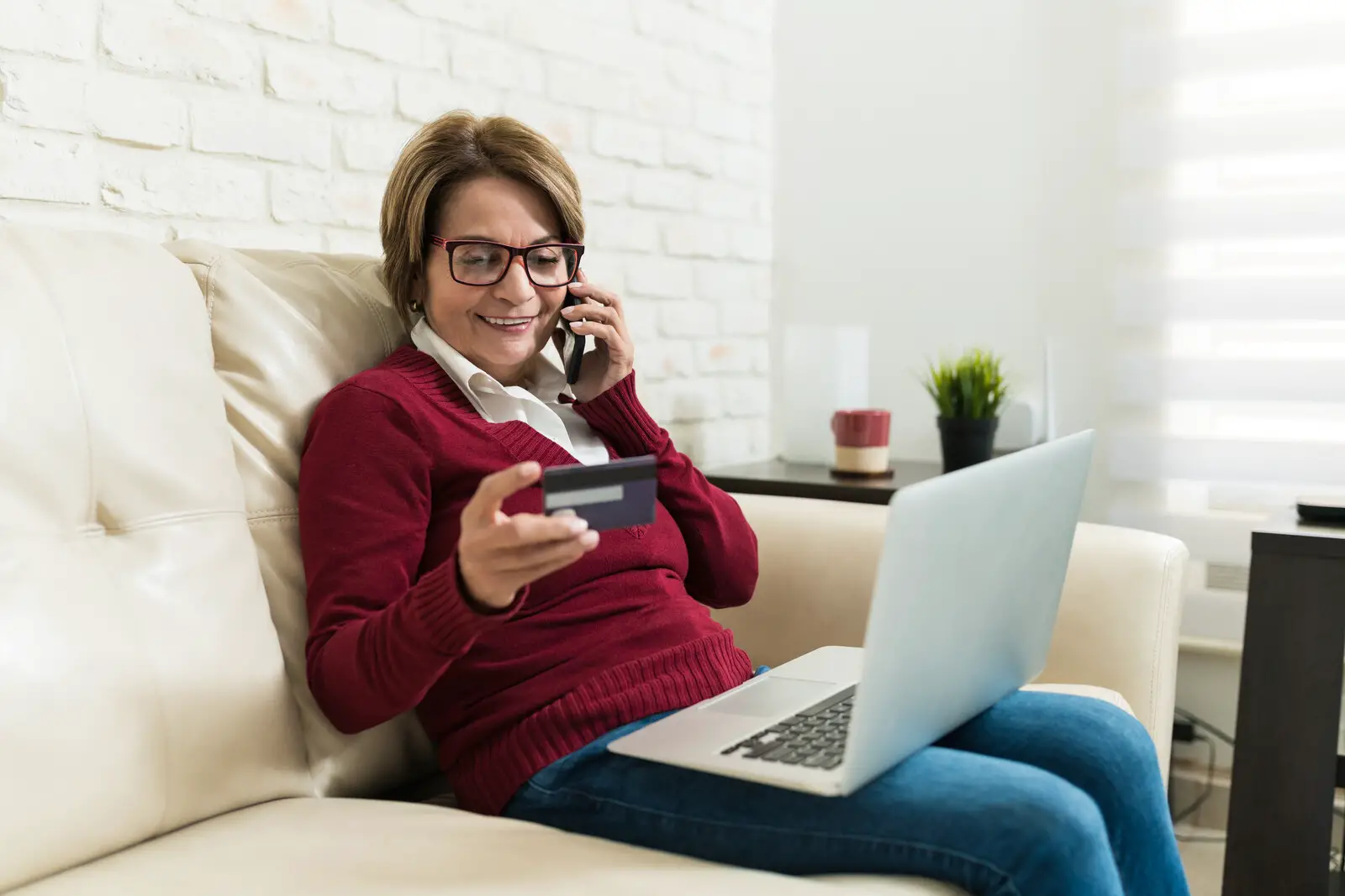 Mature woman smiling sitting on the couch giving her credit card number over the phone