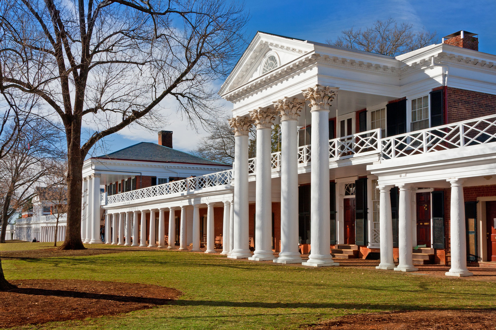 Academical village at the university of Virginia, long brick apartment building with large white pillars and balcony, blue skies and green grass.