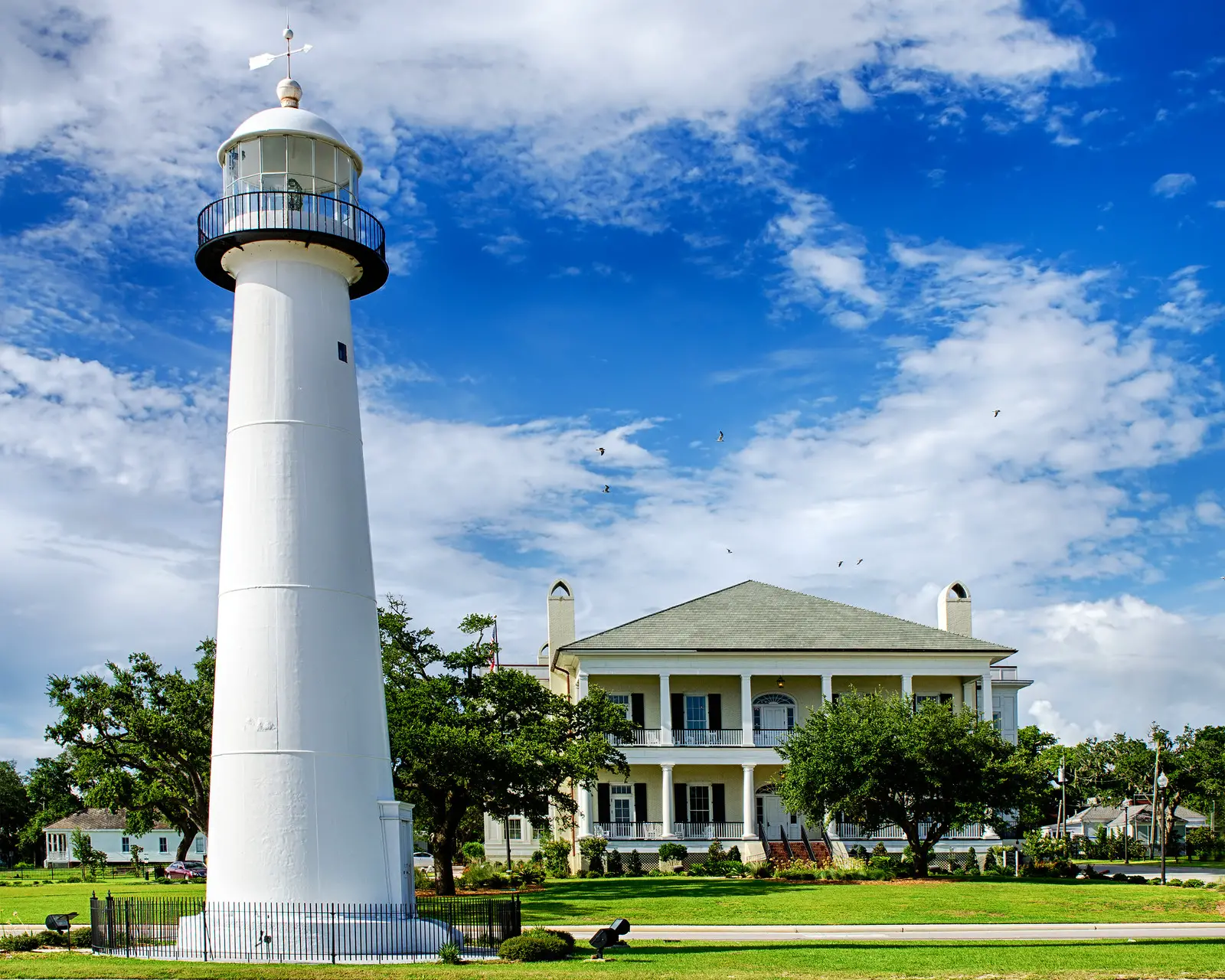 Bright blue skies with bright white clouds, green grass and the historic landmark lighthouse with the welcome back center in the background in Biloxi