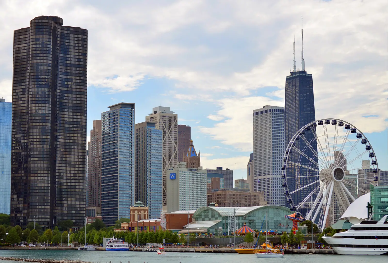 Downtown Chicago on a sunny day with blue skies at navy pier with the Ferris wheel, docked luxury shop, and bright umbrellas on the river