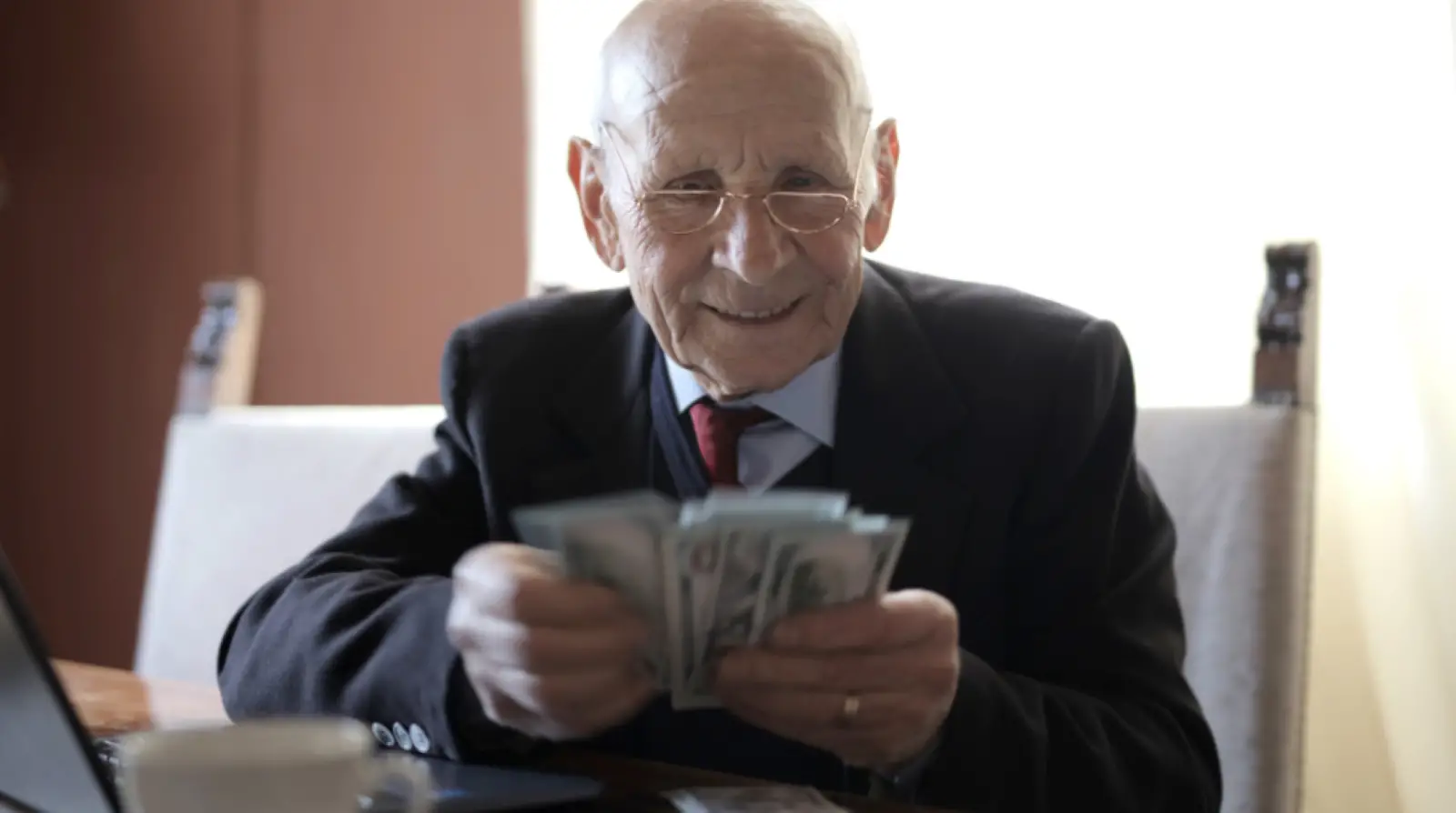Senior man smiling counting cash at his laptop