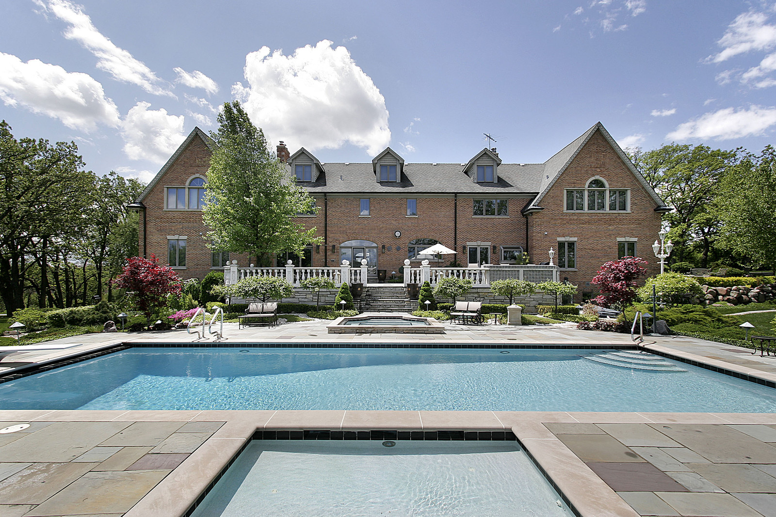 Sunny summer day, large brick house with ornate patio and large rectangle pool with adjoining square hot tub
