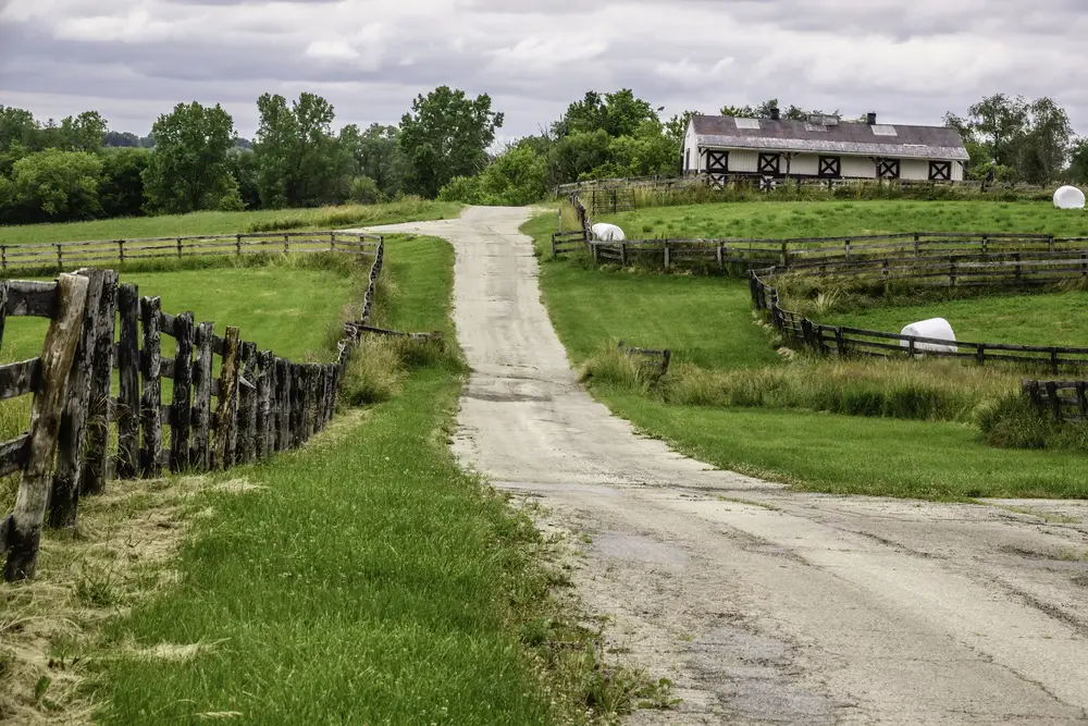 A paved road in Barrington Illinois with green meadows and a farm building