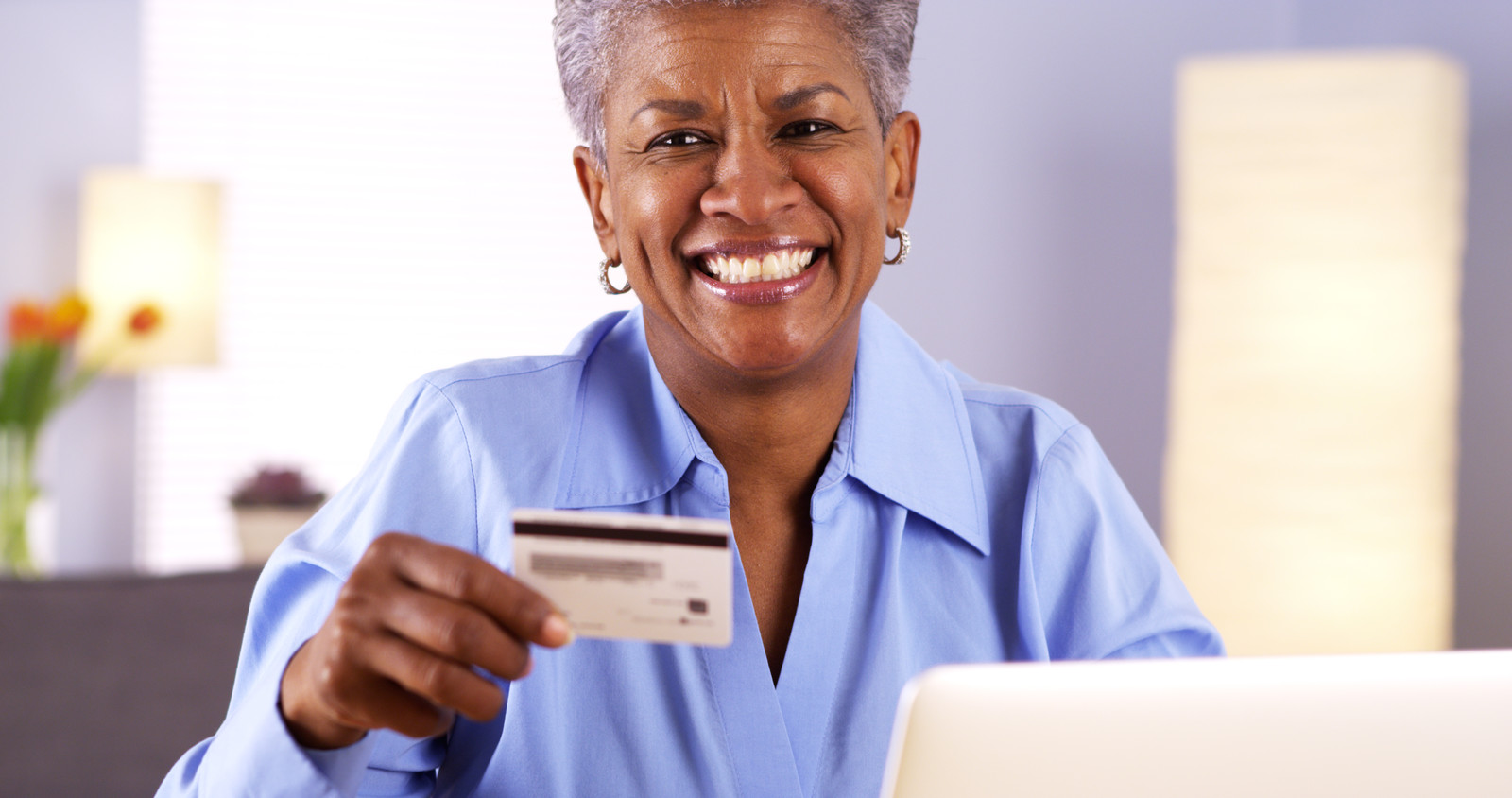Happy senior woman at home giving credit card number on laptop
