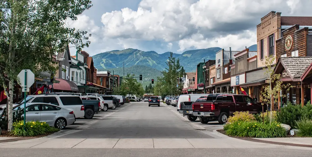 Looking straight down the main street of Whitefish Montana with cars parked on either side, blue skies, and clouds