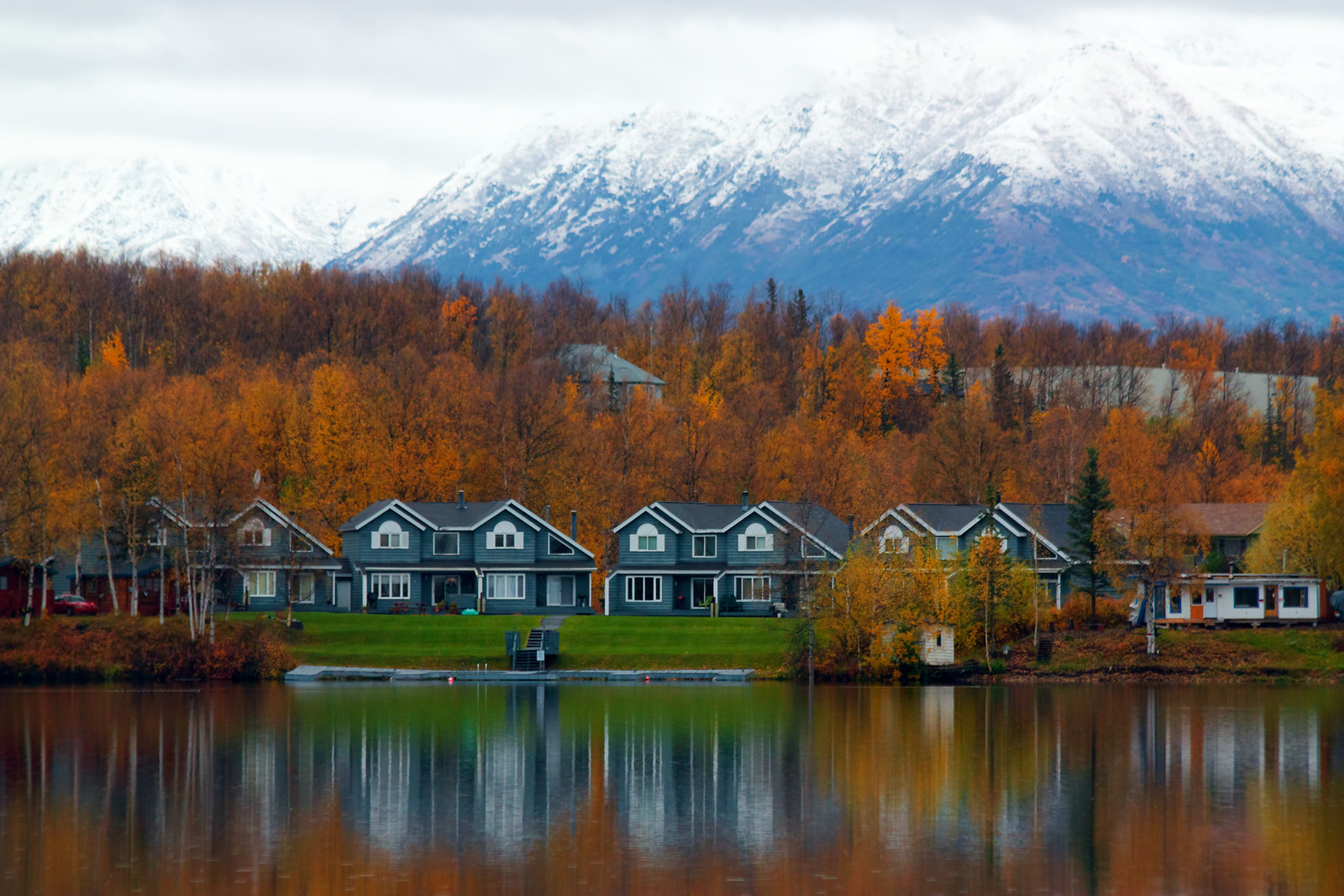 Homes On The Shore Of Lake In Wasilla With The Mountains In The Background Surrounded By Autumn Colored Trees 